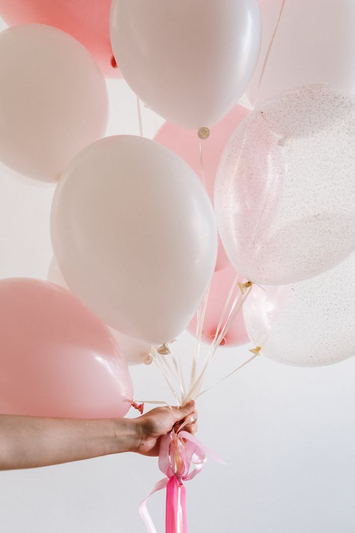 A pastel pink and white balloon bouquet held by a hand against a light background, ideal for celebrations.